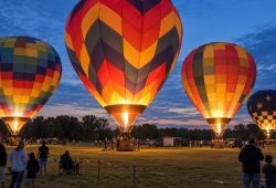 Colorful hot air balloons glowing above an open field at dusk